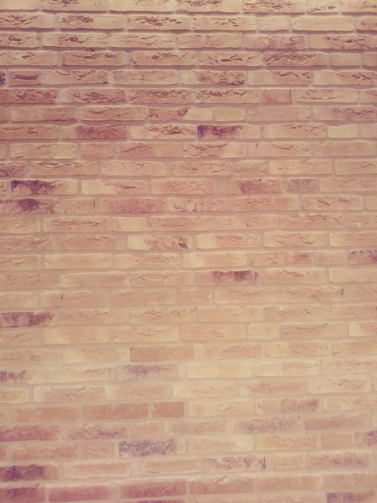 Ściana z cegły klinkierowej w odcieniach beżu i brązu, z widoczną fakturą i nieregularnymi przebarwieniami, oświetlona miękkim, rozproszonym światłem.