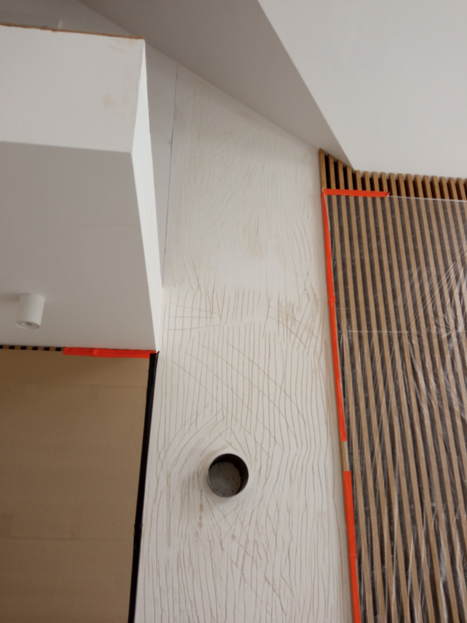 Ściana z nałożoną strukturą, widoczne ślady po narzędziach, otwór na gniazdko, listwy drewniane zabezpieczone folią, pomarańczowa taśma malarska.