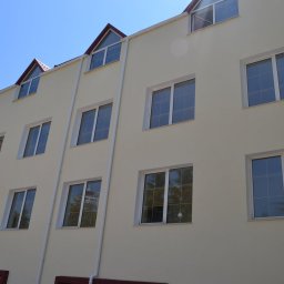 Denys Denysov - Elewacja budynku wielorodzinnego w jasnym odcieniu z białymi oknami i rynnami, widoczne trójkątne okna na poddaszu i fragment czerwonego dachu