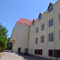 Denys Denysov - Jasny, trzypiętrowy budynek z czerwonym dachem, widoczna drabina na ścianie i sterta materiałów budowlanych przy wejściu.