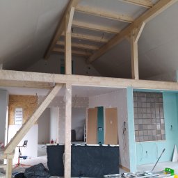 Denys Denysov - Wnętrze w trakcie prac wykończeniowych poddasza: widoczna drewniana konstrukcja stropu, częściowo obłożone płyty gipsowo-kartonowe, instalacje elektryczne, drabina i narzędzia.