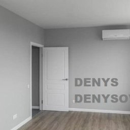 Denys Denysov - Puste pomieszczenie po remoncie w odcieniach szarości z białą cegłą na fragmencie ściany, klimatyzatorem i grzejnikiem pod oknem.