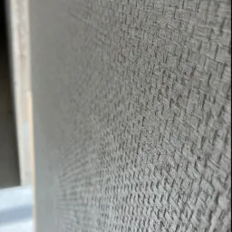 Szara tapeta o wyraźnej strukturze przypominającej tkaninę, widok z bliska z perspektywy, widoczny fragment ramy drzwi.