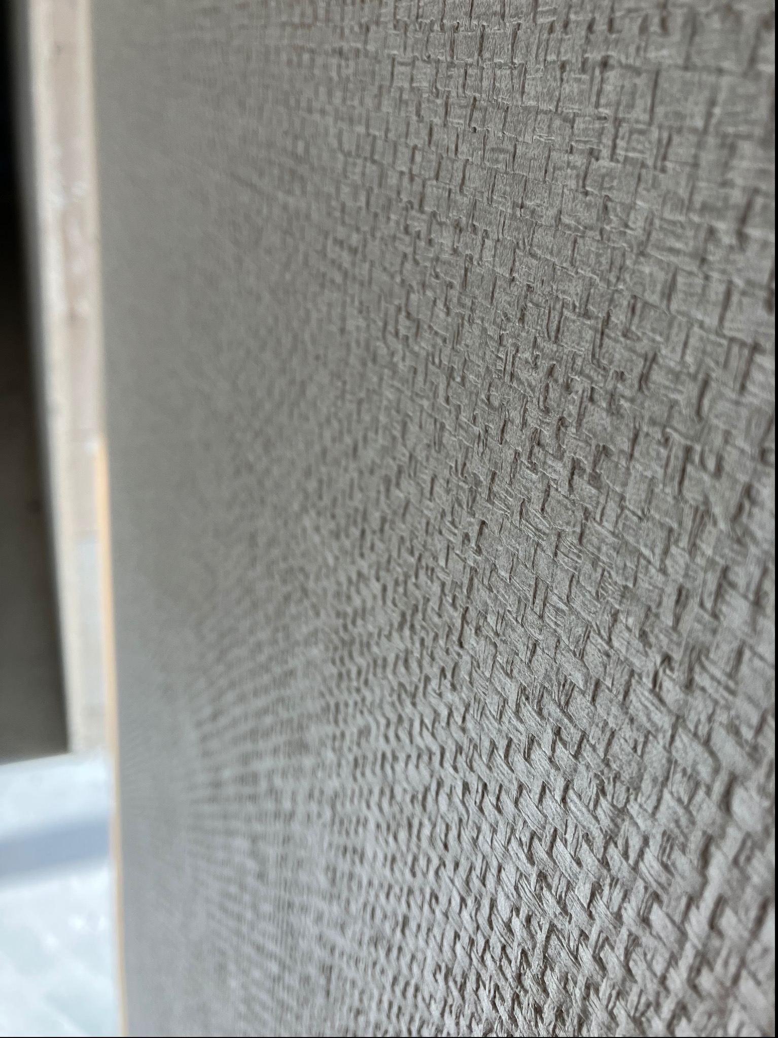 Szara tapeta o wyraźnej strukturze przypominającej tkaninę, widok z bliska z perspektywy, widoczny fragment ramy drzwi.