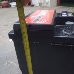 Elkom - Pomiar wysokości akumulatora samochodowego marki Perion za pomocą żółtej miarki zwijanej, widoczne oznaczenia na akumulatorze i miarce.