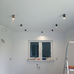 Elkom - Zamontowane punktowe oświetlenie sufitowe w nowym pomieszczeniu, widoczna drabina i przygotowane gniazdka elektryczne.