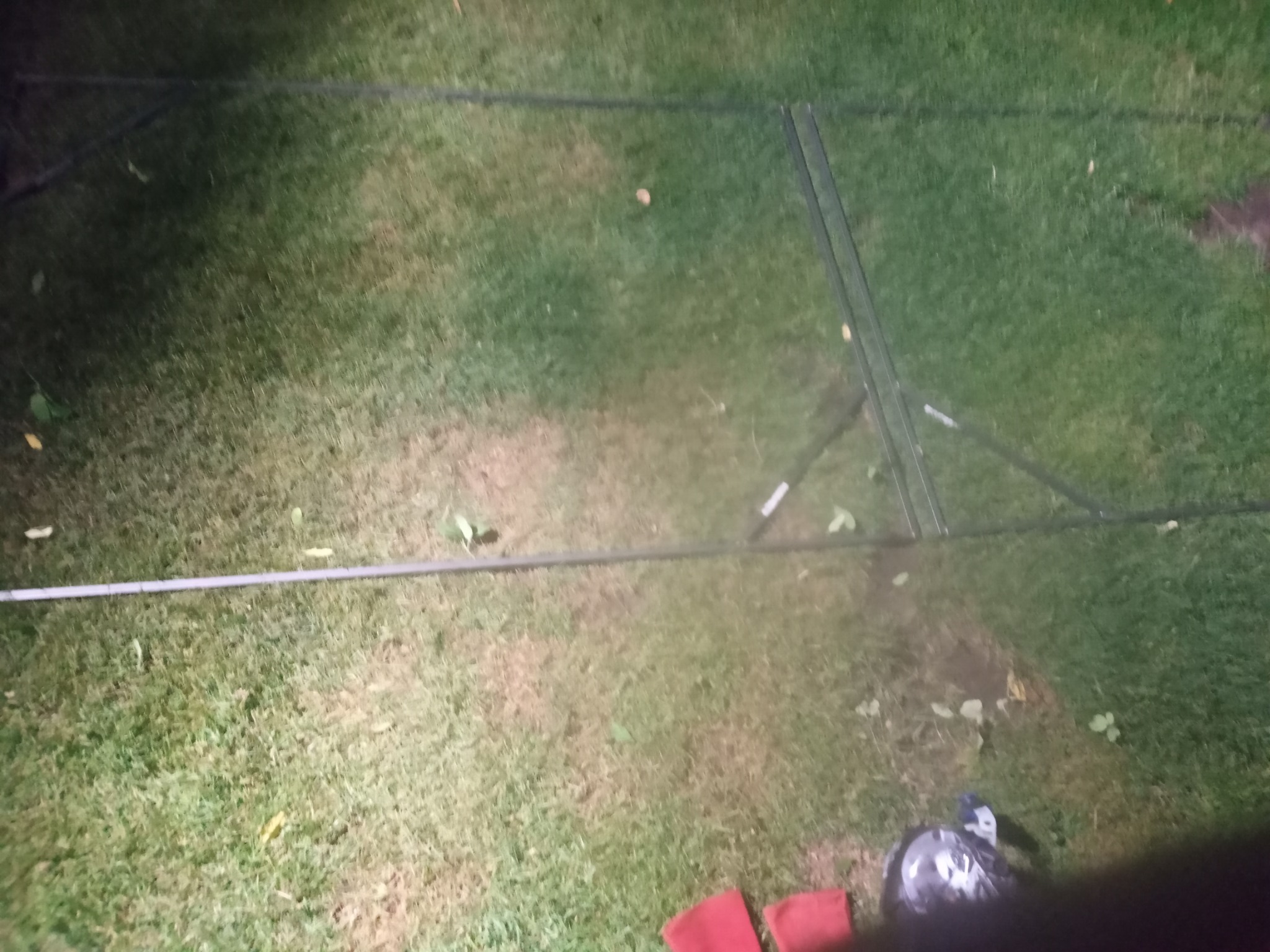 Stelaż metalowy na trawie, prawdopodobnie element instalacji odgromowej w trakcie montażu, widoczne narzędzia i fragmenty czerwonej tkaniny w rogu.