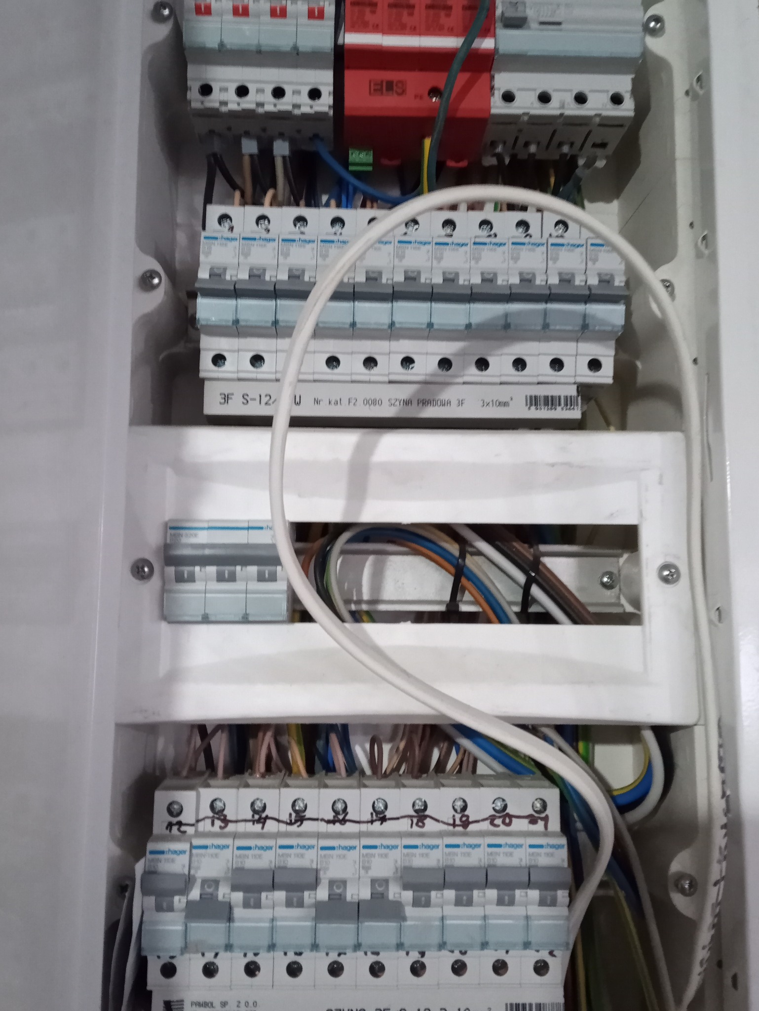 Otwarta skrzynka elektryczna z zainstalowanymi bezpiecznikami Hager, przewodami i szynami prądowymi, widoczne oznaczenia na bezpiecznikach.