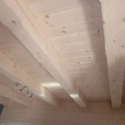 Jasne drewniane belki stropowe z widocznymi sękami i zamontowanym oświetleniem punktowym, ujęcie z dołu.