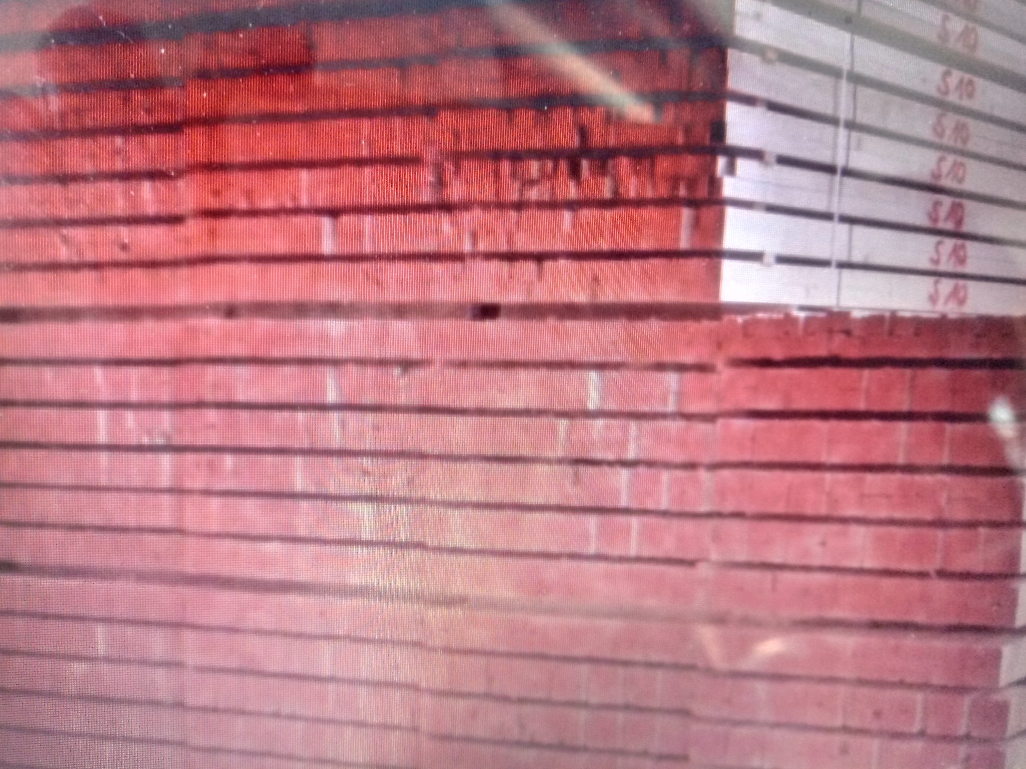 Stos czerwonych, surowych desek, częściowo zabarwionych, ułożonych warstwami, z widocznymi napisami 'S10' na niektórych elementach.