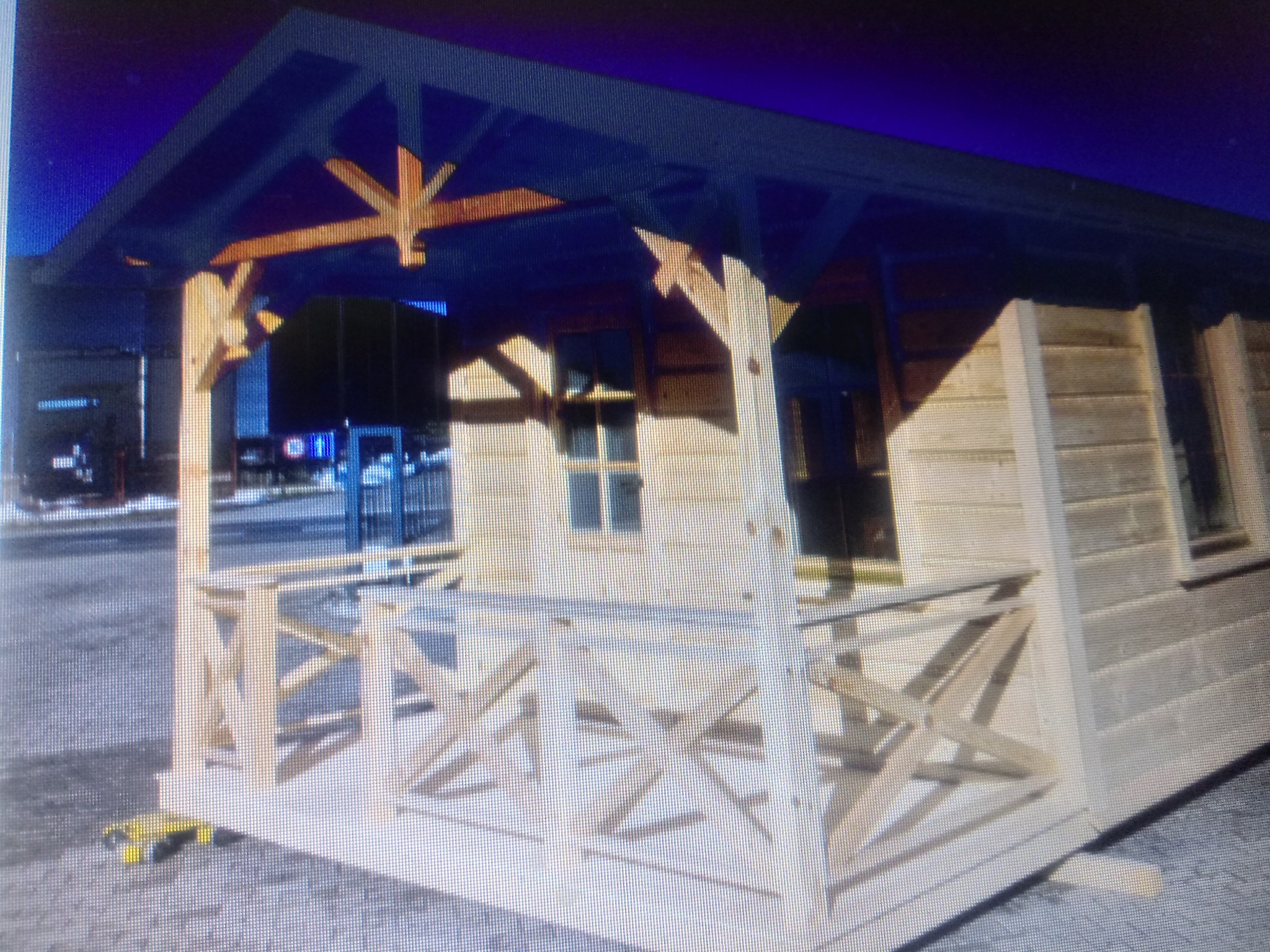 Surowa drewniana altana z widocznymi elementami konstrukcyjnymi, częściowo oszklona, na betonowej powierzchni.