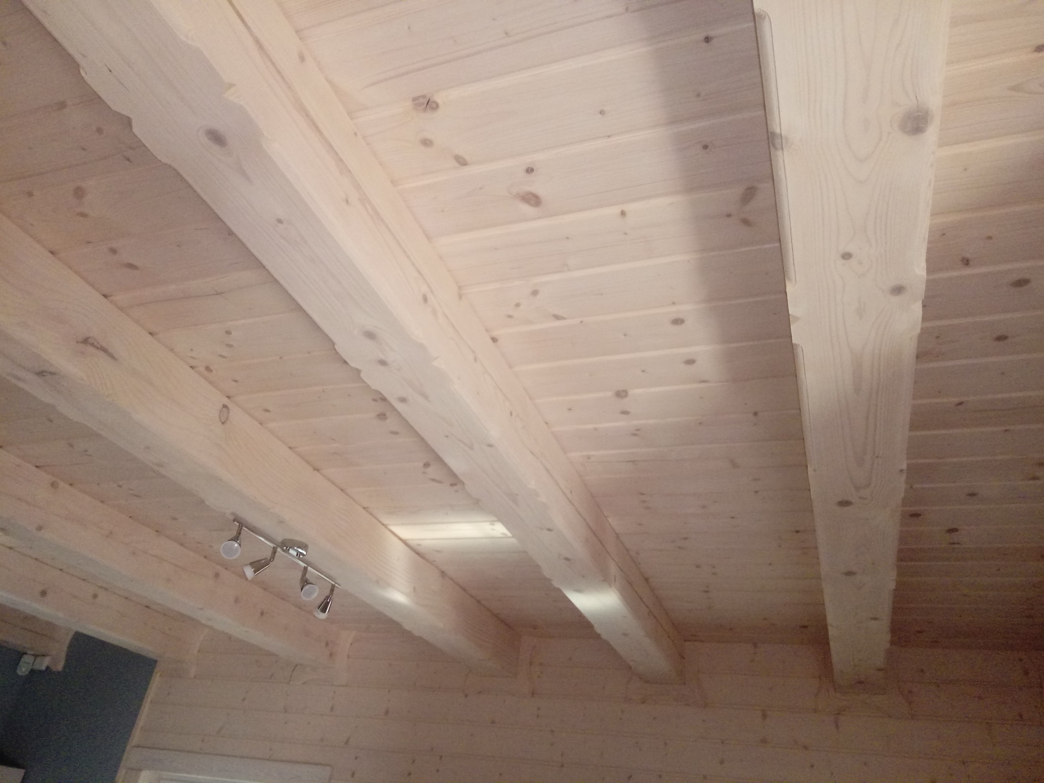 Jasne drewniane belki stropowe z widocznymi sękami i zamontowanym oświetleniem punktowym, ujęcie z dołu.