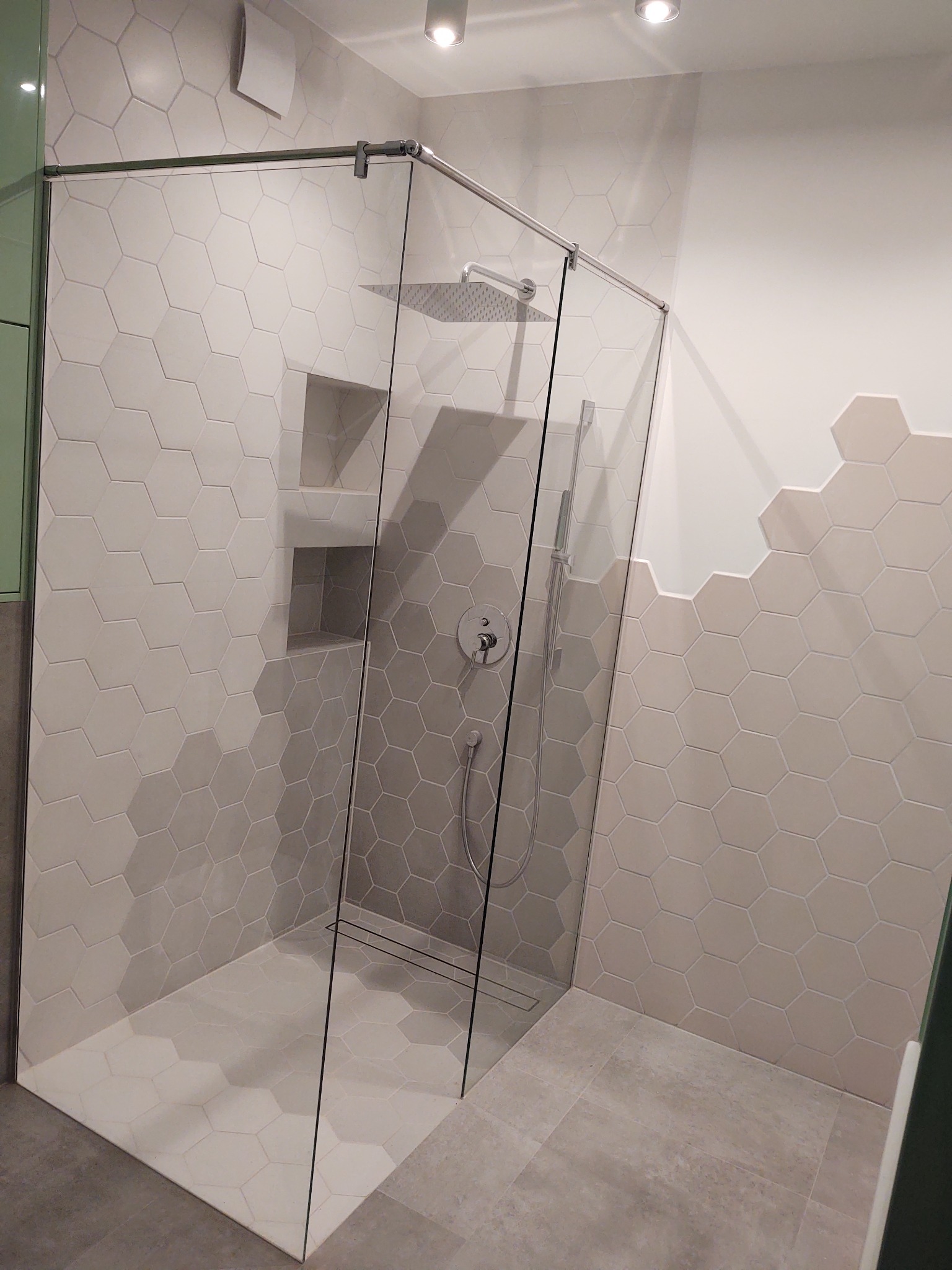 Nowoczesna kabina prysznicowa typu walk-in z geometrycznymi, heksagonalnymi płytkami w odcieniach szarości i beżu, wbudowanymi półkami w ścianie i deszczownicą.