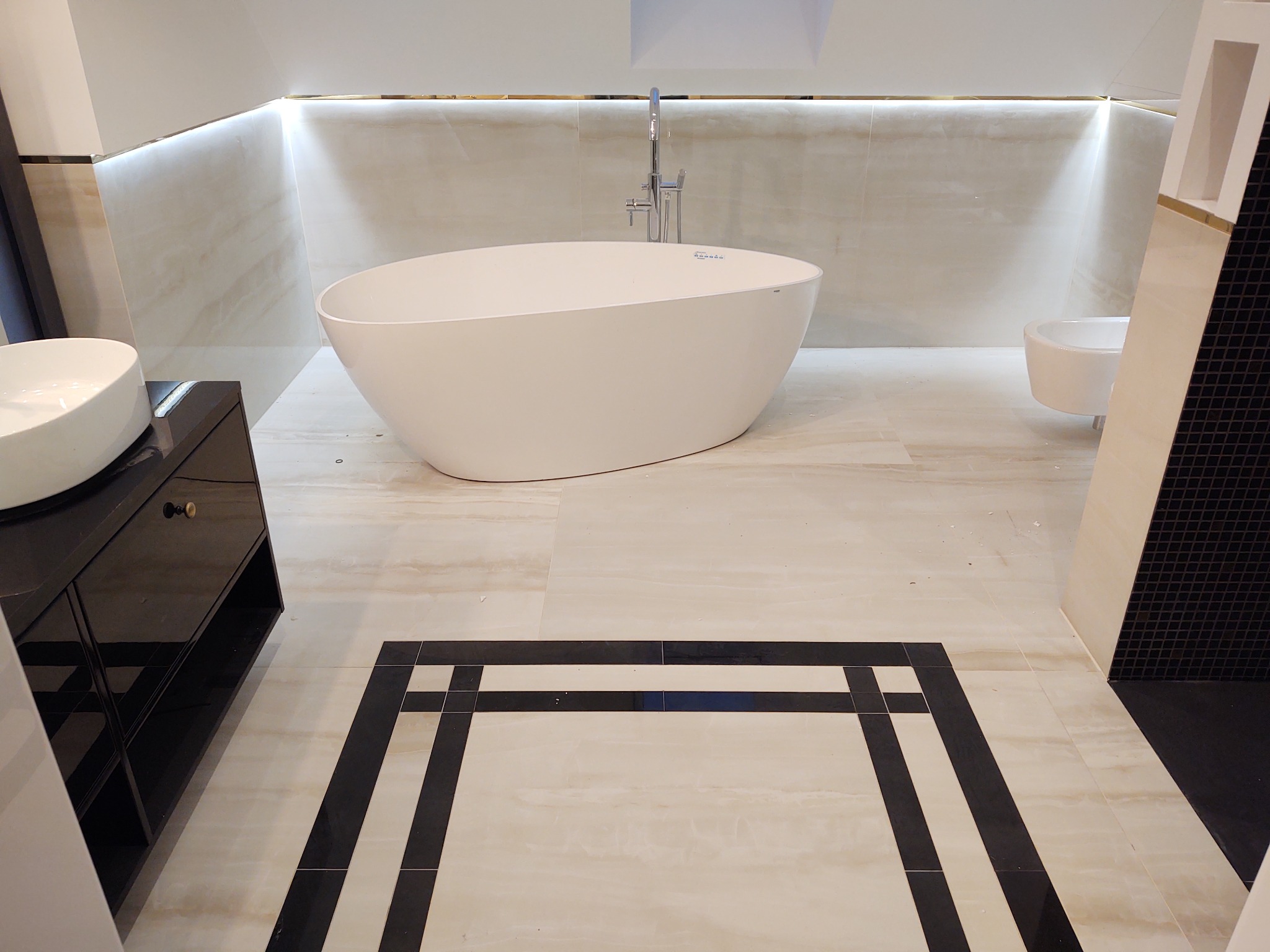 Elegancka, minimalistyczna łazienka w Stargardzie z wolnostojącą wanną, umywalką nablatową na czarnej szafce, beżowymi płytkami na ścianach i podłodze z czarną dekoracyjną ramką.