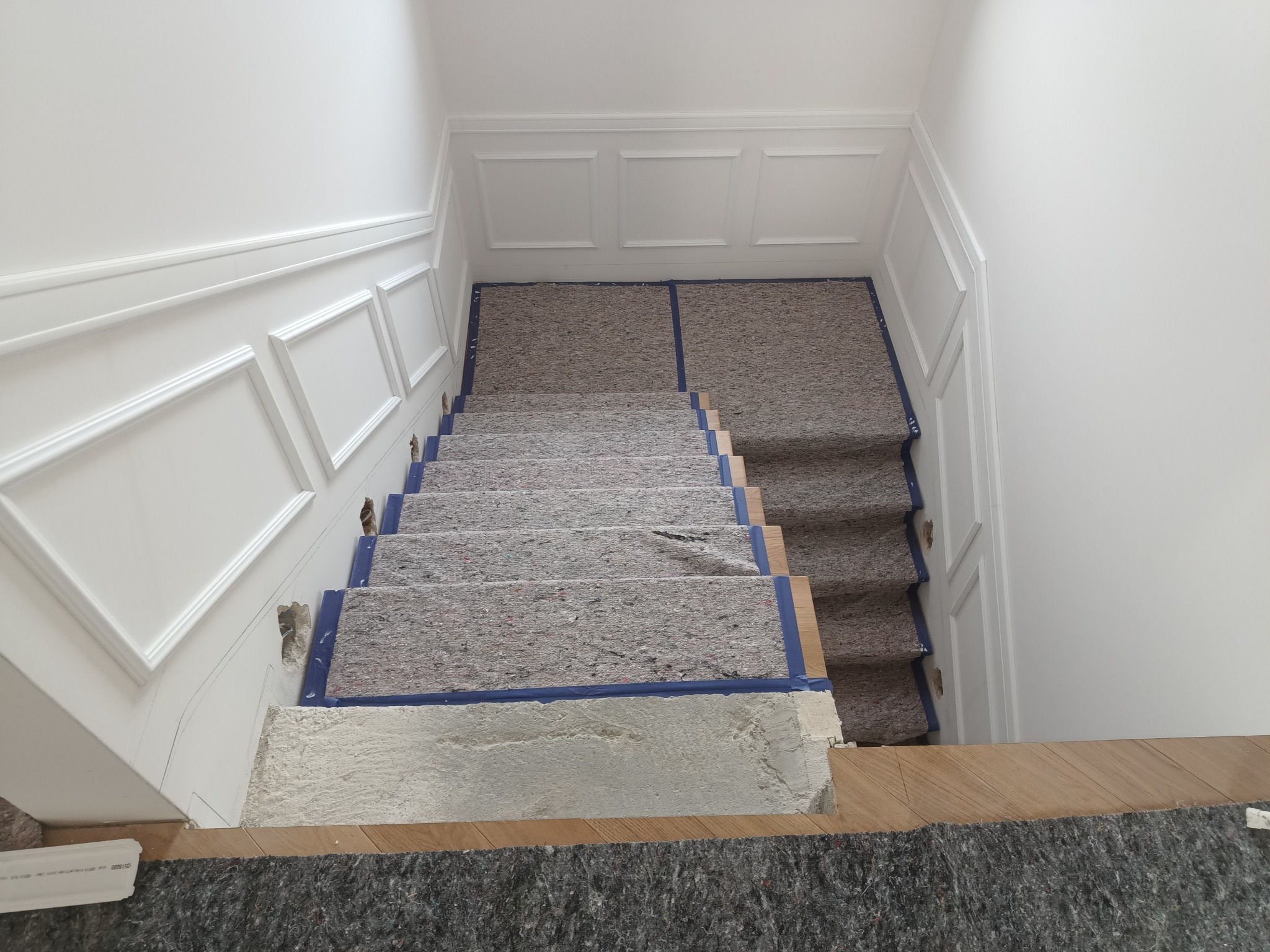 Schody w trakcie zabezpieczania przed pracami wykończeniowymi, z widocznymi elementami dekoracyjnymi na ścianach i zabezpieczeniami na stopniach.