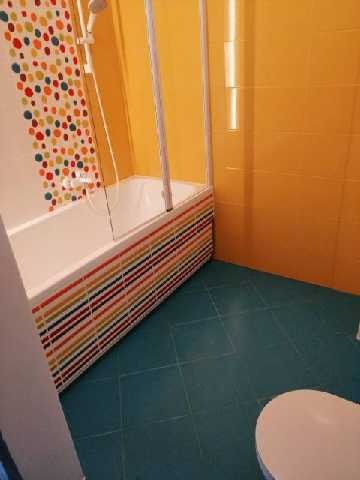 Żółto-niebieska łazienka z wanną w kolorowe paski, kabiną prysznicową i wzorzystymi płytkami na ścianie.