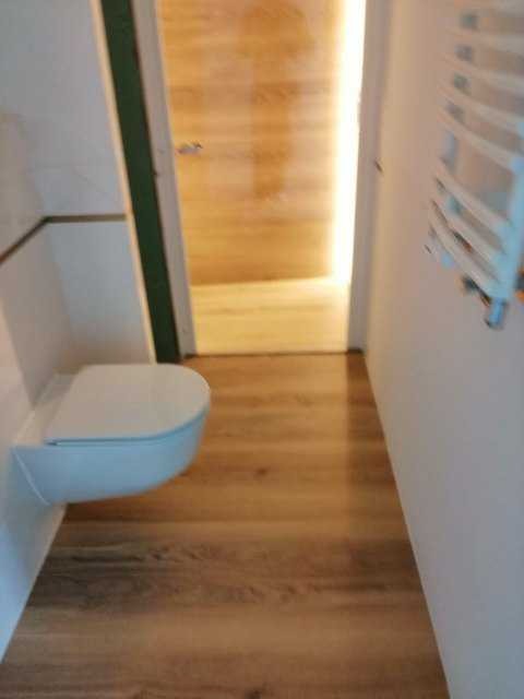 Nowoczesna toaleta podwieszana z drewnopodobną podłogą i grzejnikiem drabinkowym w wykończonym wnętrzu łazienki, widok z perspektywy podłogi.