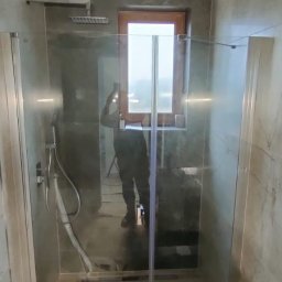 Cover AT bud Andrii Danyliuk - Nowoczesna kabina prysznicowa z deszczownicą i szklanymi drzwiami przesuwnymi, widoczna armatura i okno w drewnianej ramie w wykończonej łazience.