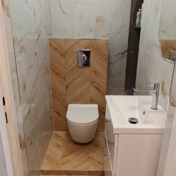 Cover AT bud Andrii Danyliuk - Nowoczesna łazienka z beżowymi płytkami imitującymi marmur i drewnopodobną podłogą ułożoną w jodełkę. Umywalka z szafką i podwieszana toaleta.