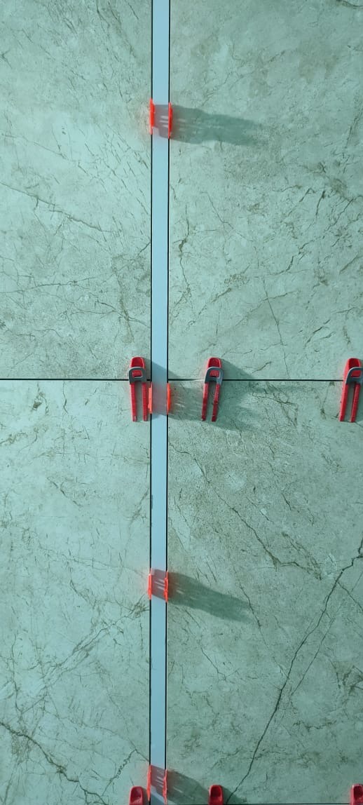 Ułożone płytki imitujące marmur z użyciem systemu poziomowania, widoczne klipsy i kliny w kolorze czerwonym, fuga w kolorze szarym.