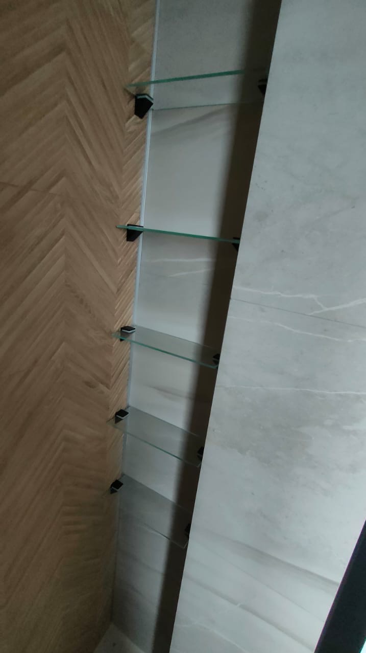 Półki szklane zamontowane na ścianie wyłożonej płytkami imitującymi drewno w jodełkę i marmurowe płyty w łazience.