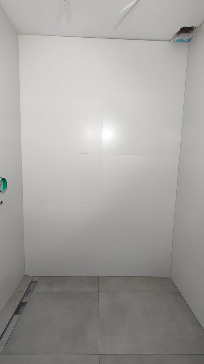 Świeżo wykafelkowana ściana w łazience z widocznym odpływem liniowym w podłodze i niedokończonym fragmentem sufitu.