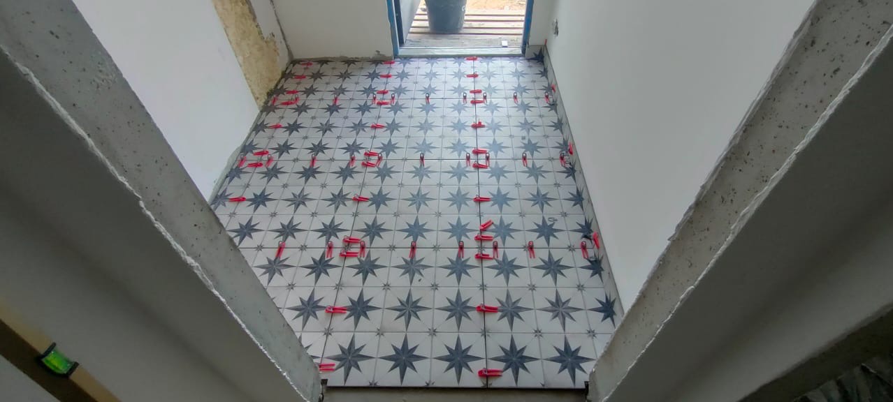 Ułożona podłoga z płytek w gwiazdy, z czerwonymi klipsami poziomującymi, widok z góry na świeżo wykończoną posadzkę w pomieszczeniu w trakcie remontu.