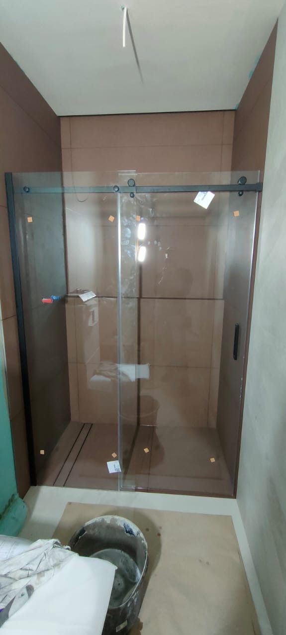 Nowoczesna kabina prysznicowa z przesuwnymi drzwiami, wykończona brązowymi płytkami. Widoczny fragment wiadra i zabezpieczeń na szkle.