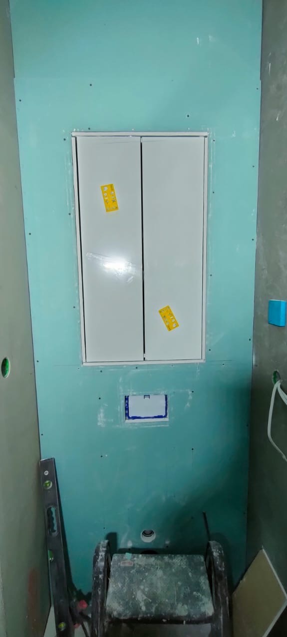 Płyty GK na ścianie z zamontowanym rewizyjnym włazem. Widoczne narzędzia i niedokończone wykończenie. Etap prac w trakcie remontu łazienki.