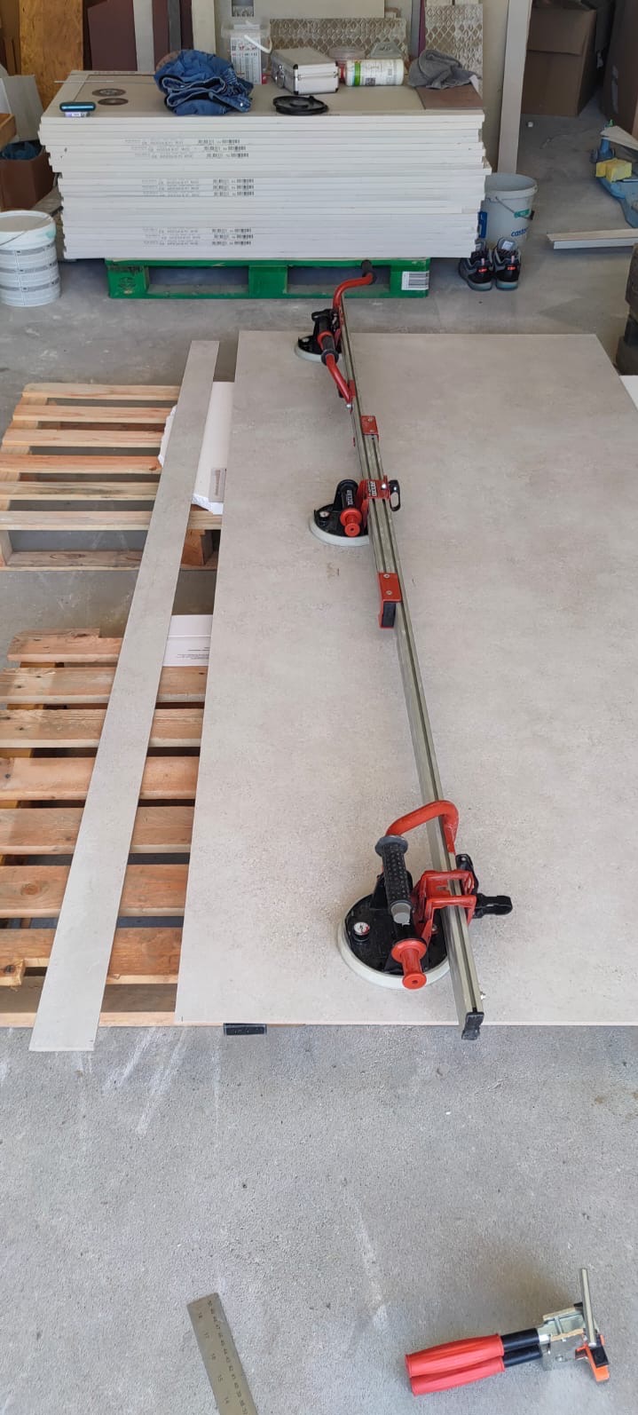 Przygotowanie do cięcia płytki wielkoformatowej za pomocą specjalistycznej przecinarki z przyssawkami. W tle paleta z płytami gipsowo-kartonowymi.