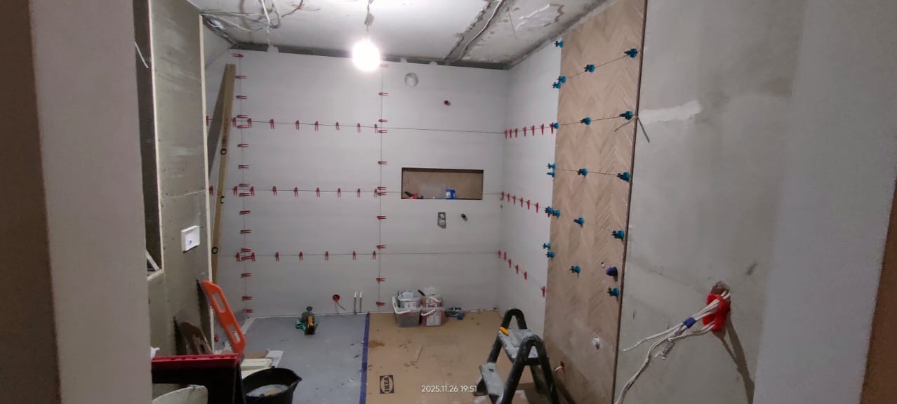 Remont łazienki w trakcie: częściowo ułożone płytki w jodełkę, poziomice, krzyżyki dystansowe, przygotowane ściany. Widoczne narzędzia i materiały budowlane.