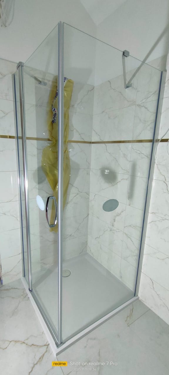 Nowoczesna kabina prysznicowa z chromowanymi profilami i marmurowymi płytkami. Widoczny brodzik i szklane drzwi. Wnętrze kabiny częściowo zasłonięte folią ochronną.