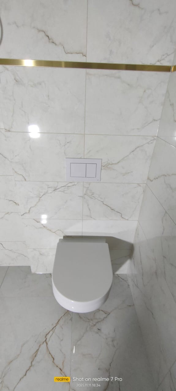 Biała toaleta wisząca z podtynkową spłuczką na tle marmurowych płytek z złotym akcentem. Minimalistyczny design łazienki po remoncie, widok z góry.