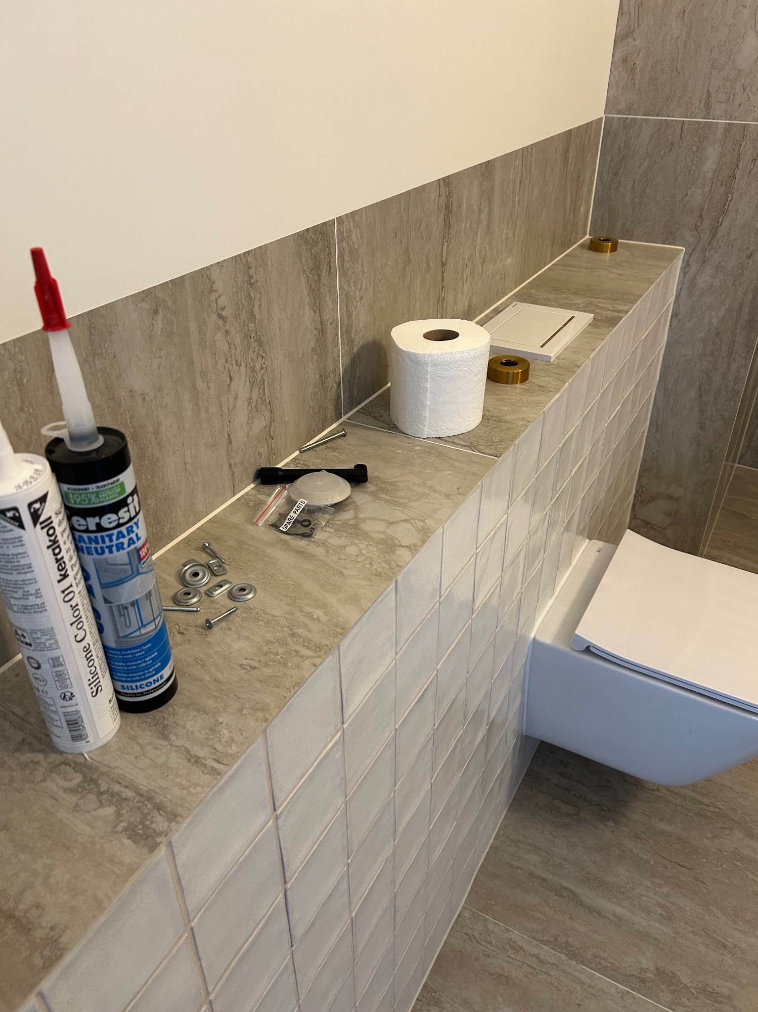 Podwieszana toaleta w trakcie montażu: widoczne silikony, śruby i płytki imitujące marmur. Ujęcie z bliska na etapie prac wykończeniowych w łazience.