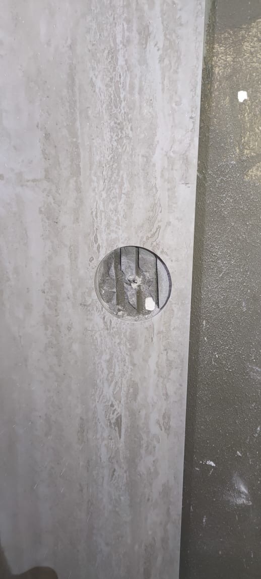 Płytka imitująca marmur z wyciętym otworem na puszkę elektryczną, widoczne przewody. Przygotowanie do montażu gniazdka w wykończonej ścianie.