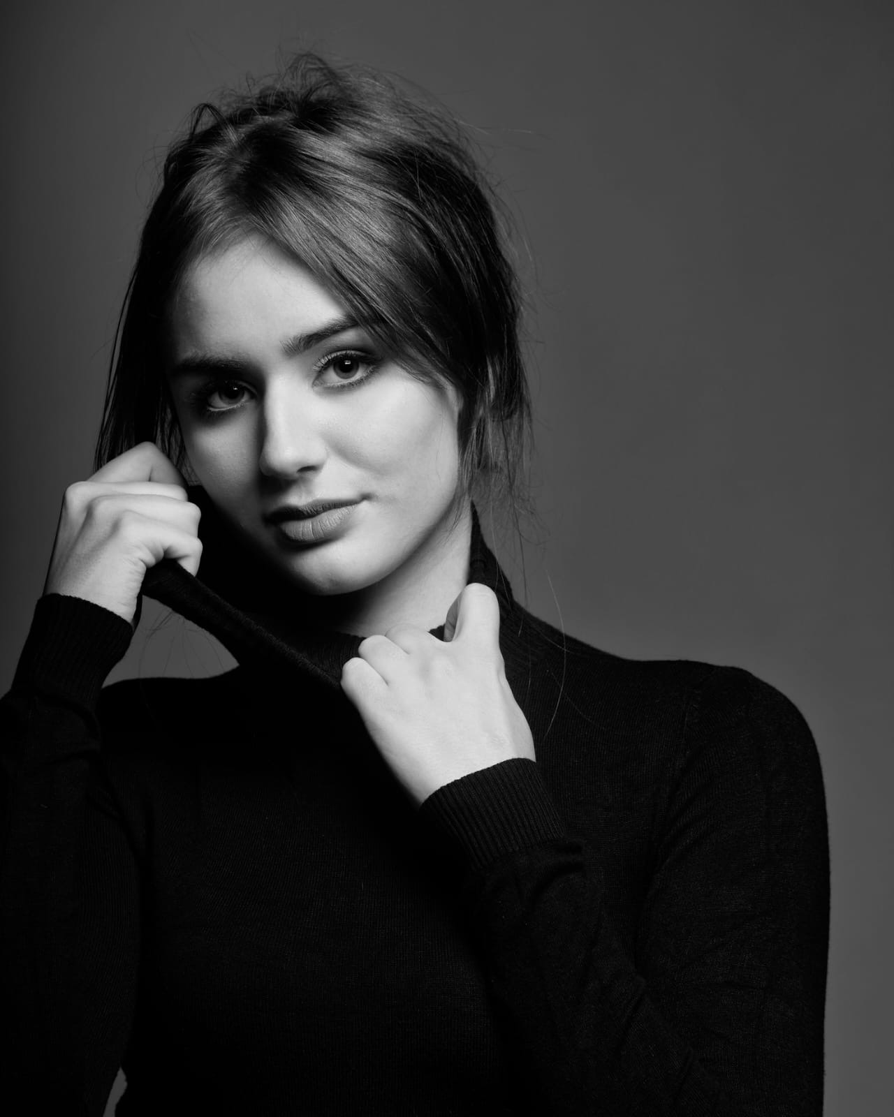Czarno-biały portret młodej kobiety w czarnym golfie na szarym tle, wykonany w Rosanowie, z delikatnym oświetleniem podkreślającym rysy twarzy i fakturę materiału.