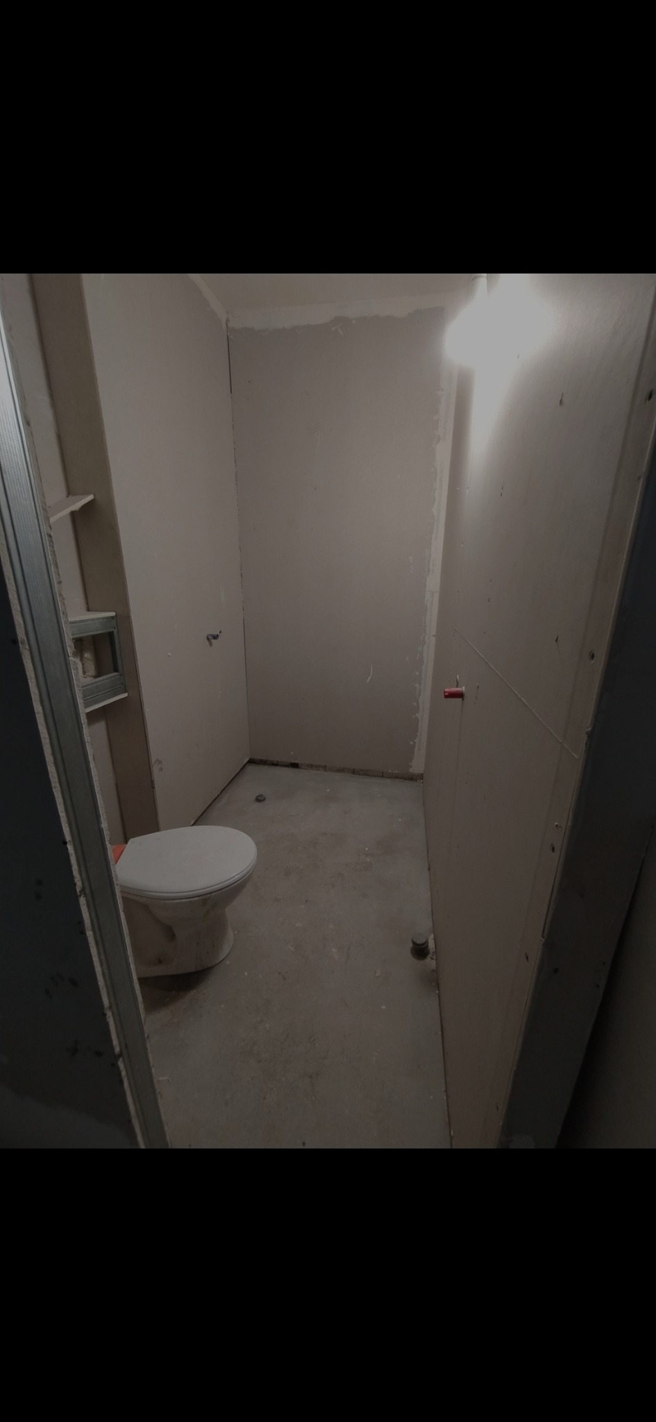 Łazienka w trakcie remontu: widoczne ściany z płyt kartonowo-gipsowych, surowa podłoga i zamontowana toaleta. Metalowy stelaż pod zabudowę.