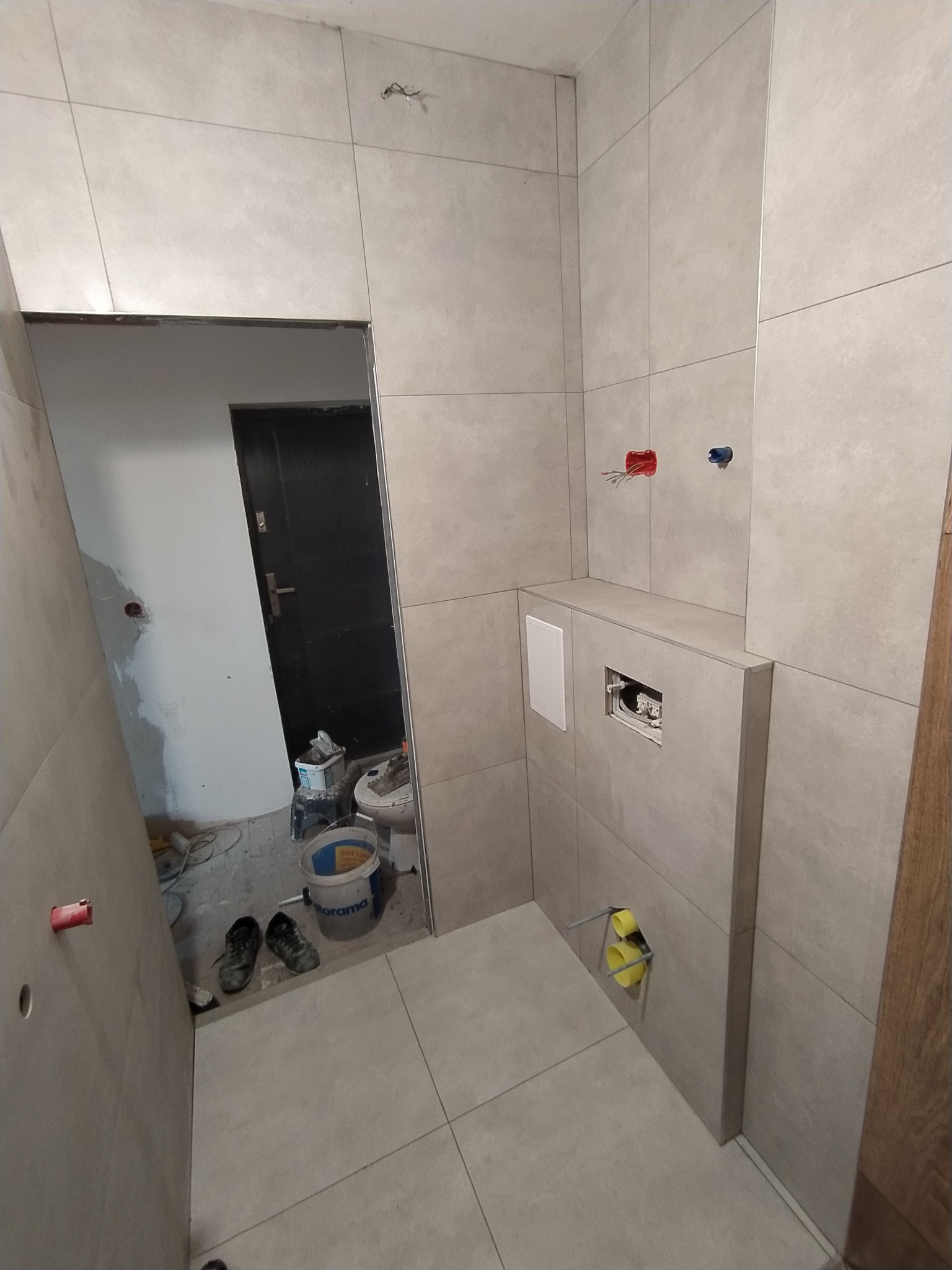 Wnętrze łazienki w trakcie remontu w Bytomiu, widoczne szare płytki na ścianach i podłodze, przygotowane instalacje wodno-kanalizacyjne, z elementami instalacji podtynkowych i akcesoriami...