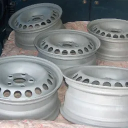 Cztery stalowe felgi samochodowe po renowacji, pomalowane na srebrno, ułożone na kocu w bagażniku pojazdu.