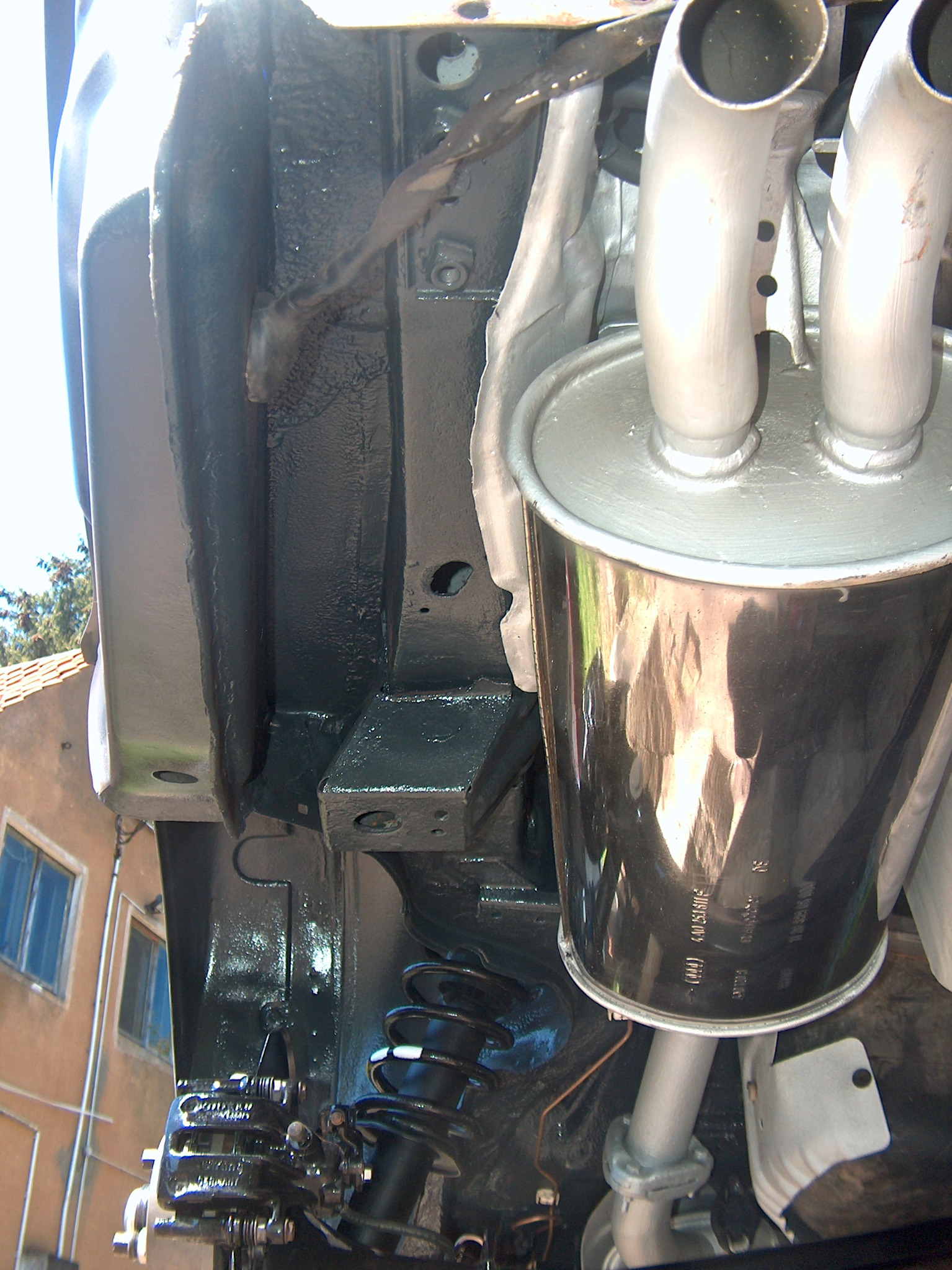 Podwozie samochodu po konserwacji antykorozyjnej: pomalowane elementy zawieszenia, tłumik i karoseria. Widok od dołu, z zewnątrz budynku.