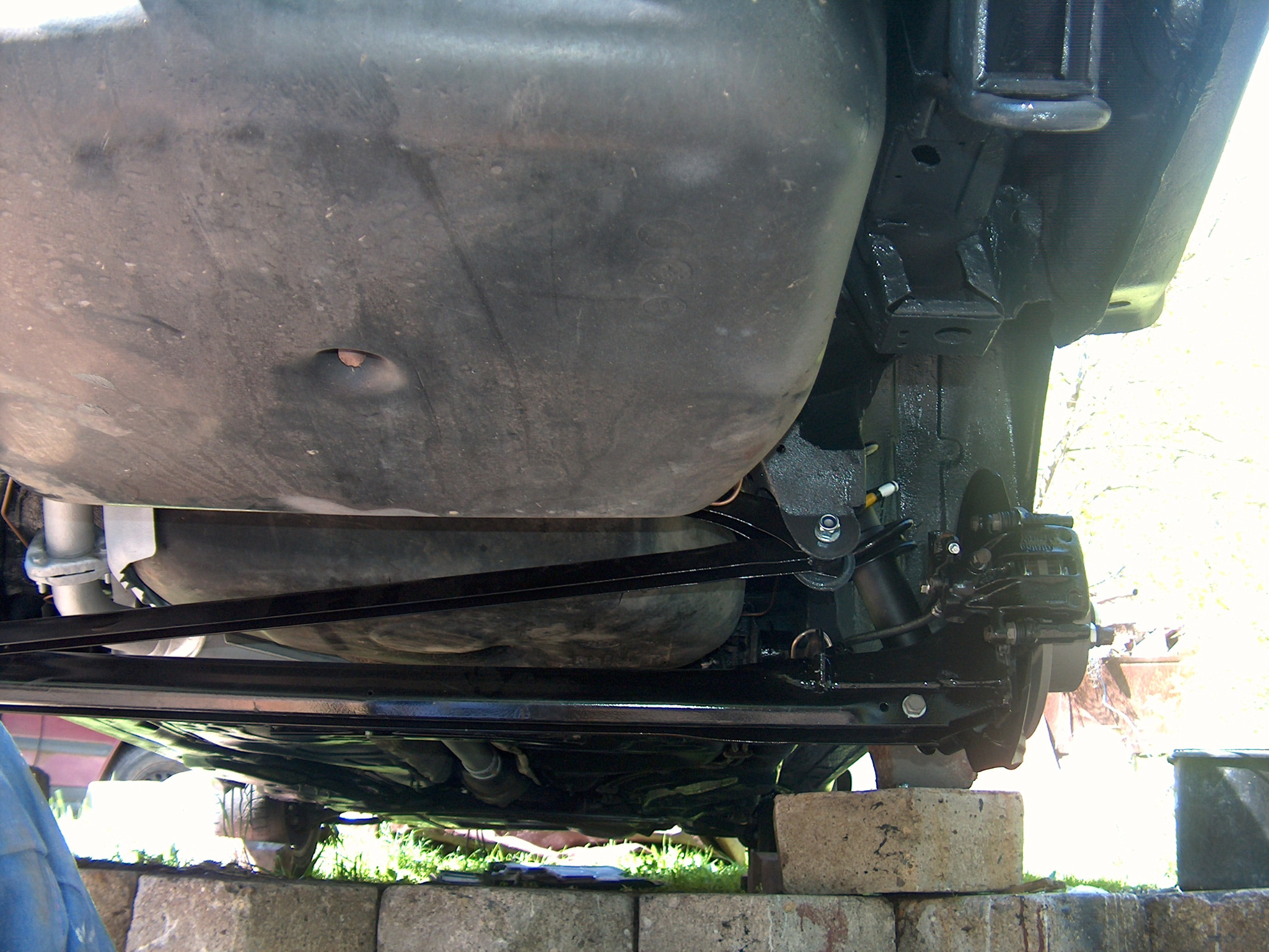 Podwozie auta po konserwacji, widok z dołu. Elementy zawieszenia i układ hamulcowy pomalowane na czarno. Auto stoi na betonowych blokach.