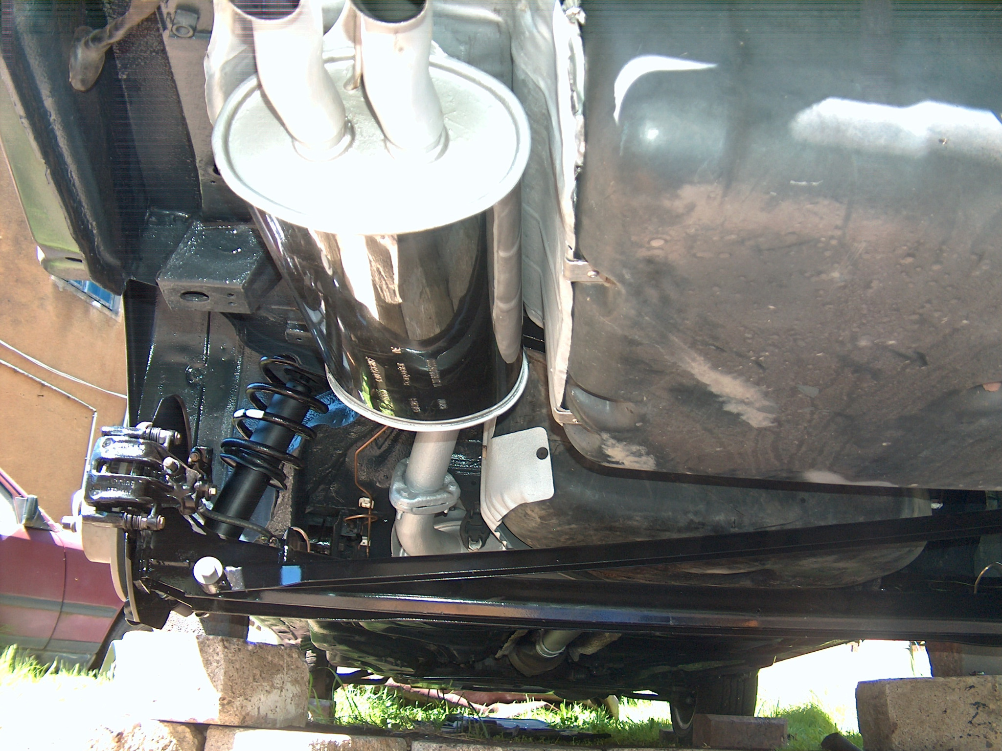 Podwozie samochodu po konserwacji: świeżo pomalowane elementy zawieszenia, nowy tłumik. Auto podniesione na betonowych blokach.