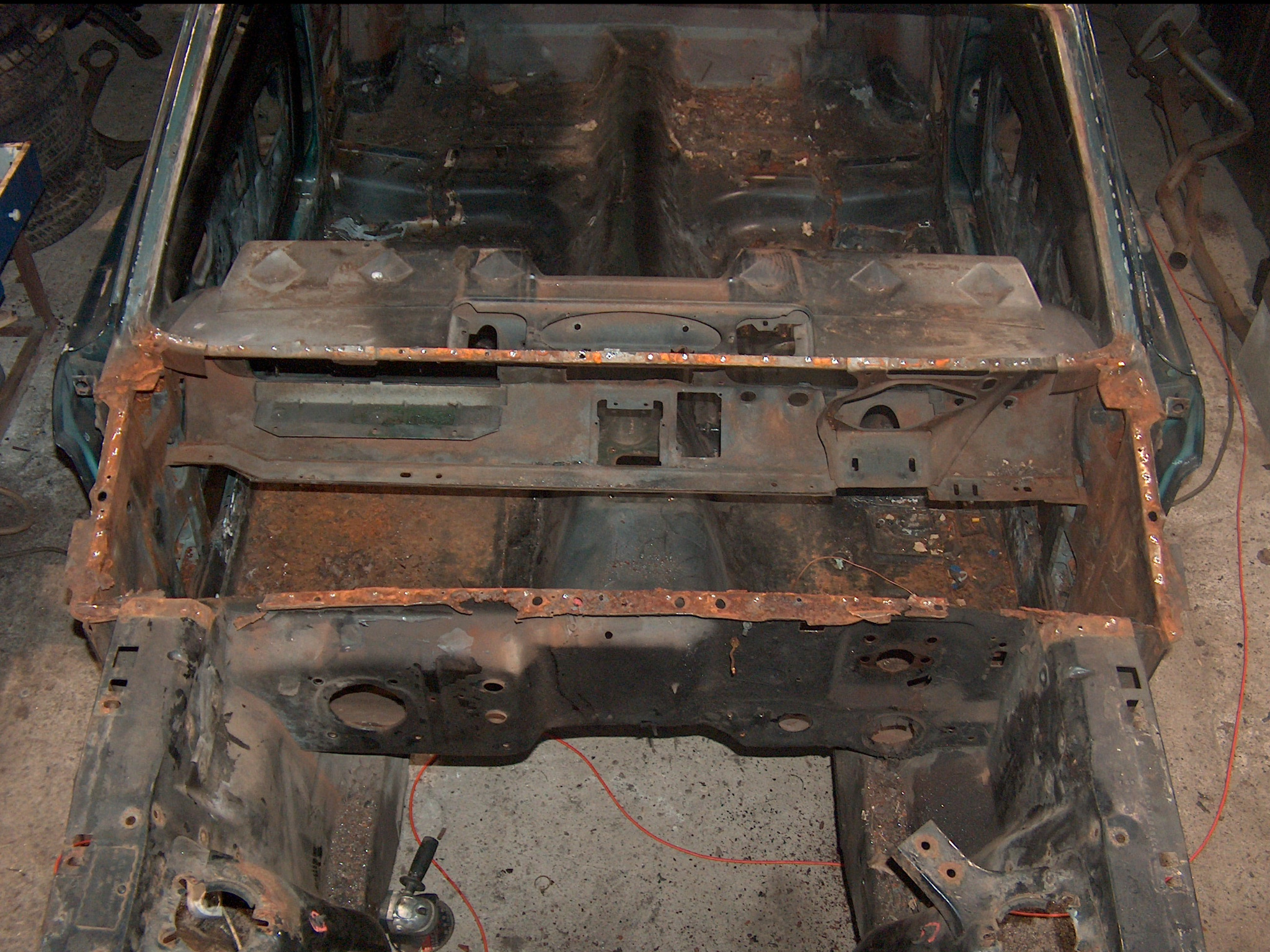 Zdemontowane nadwozie samochodu w trakcie renowacji, widoczne ślady korozji i spawania. Elementy metalowe przygotowane do dalszej obróbki.