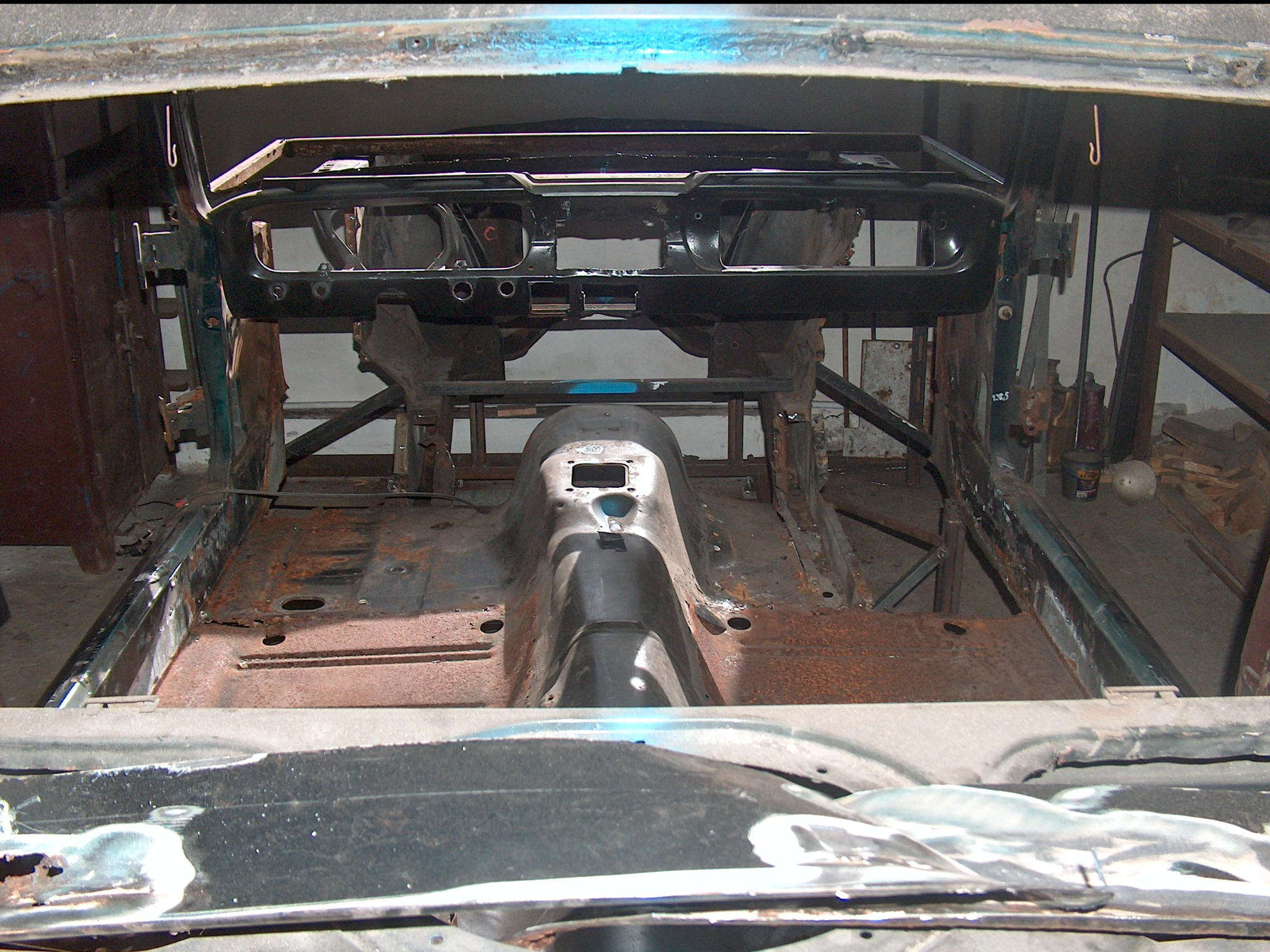 Wnętrze karoserii samochodu w trakcie renowacji. Widoczne elementy metalowe, częściowo skorodowane, przygotowywane do dalszej obróbki i zabezpieczenia antykorozyjnego.