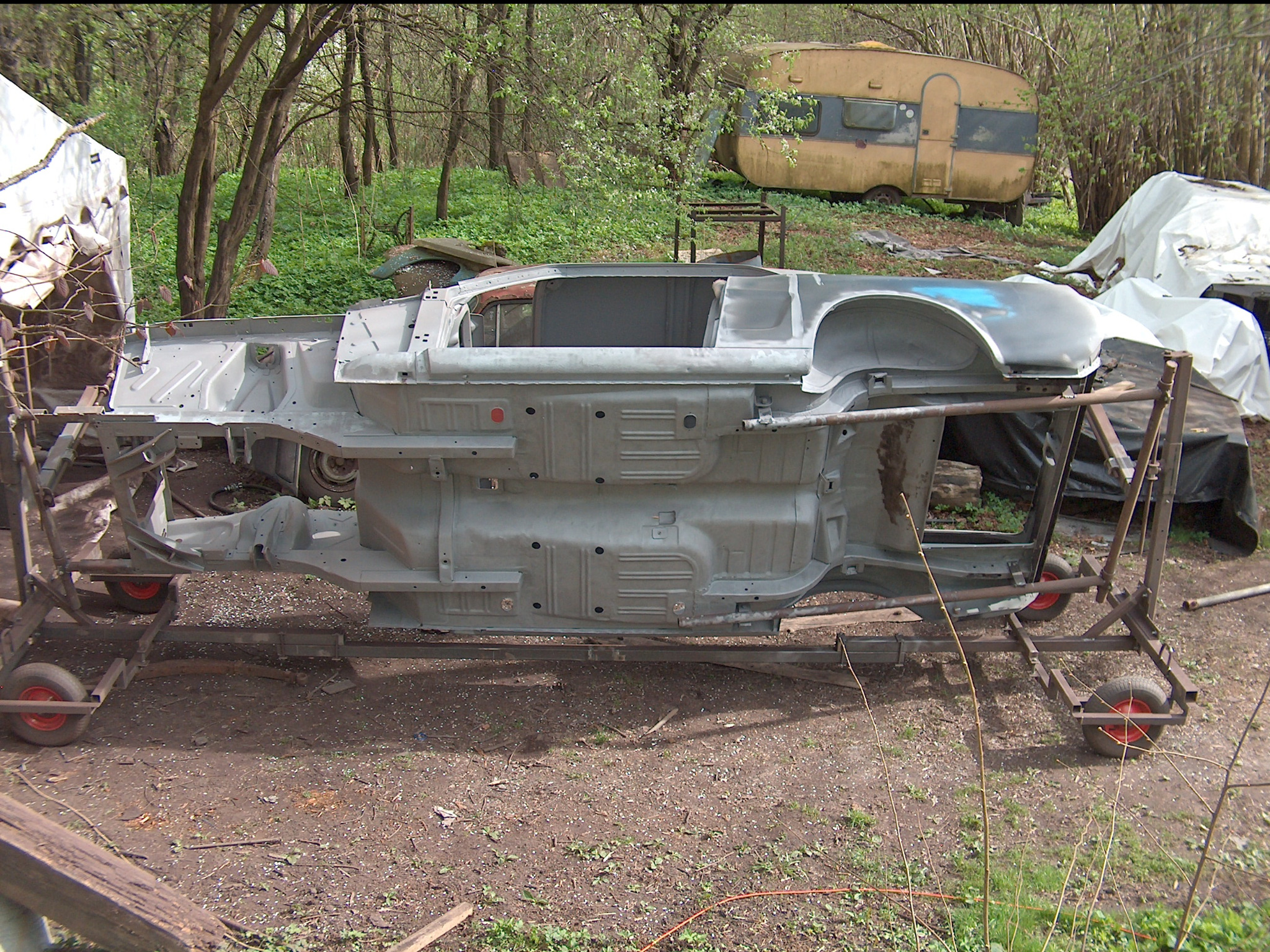 Karoseria samochodu po odnowieniu, umieszczona na wózku w otoczeniu drzew. Widoczny szkielet pojazdu w szarym kolorze, z elementami wnętrza i podwozia.