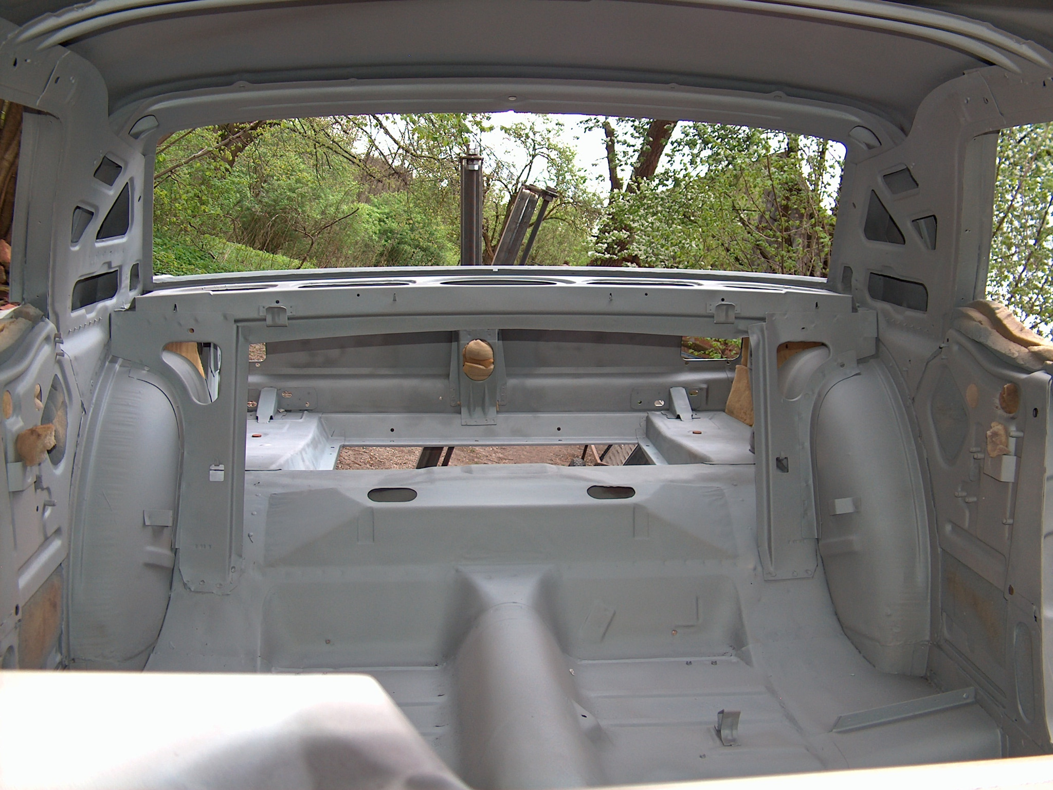 Wnętrze karoserii auta po piaskowaniu i zabezpieczeniu antykorozyjnym, widoczne otwory i wzmocnienia. Tło stanowi zieleń drzew.
