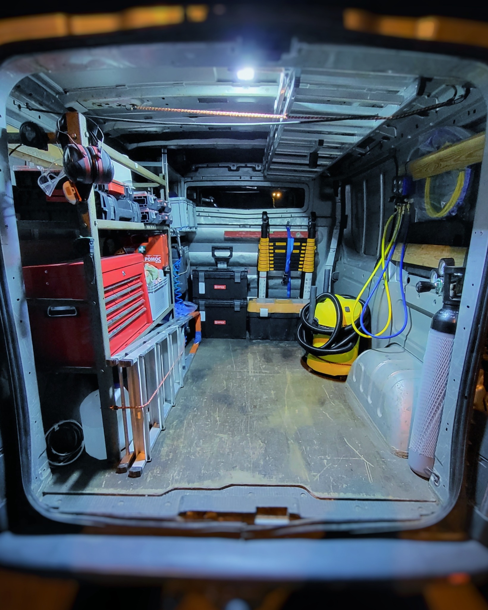 Wnętrze furgonetki serwisowej z narzędziami, skrzynkami, drabiną teleskopową, butlą z gazem technicznym oraz odkurzaczem przemysłowym, wszystko starannie poukładane.