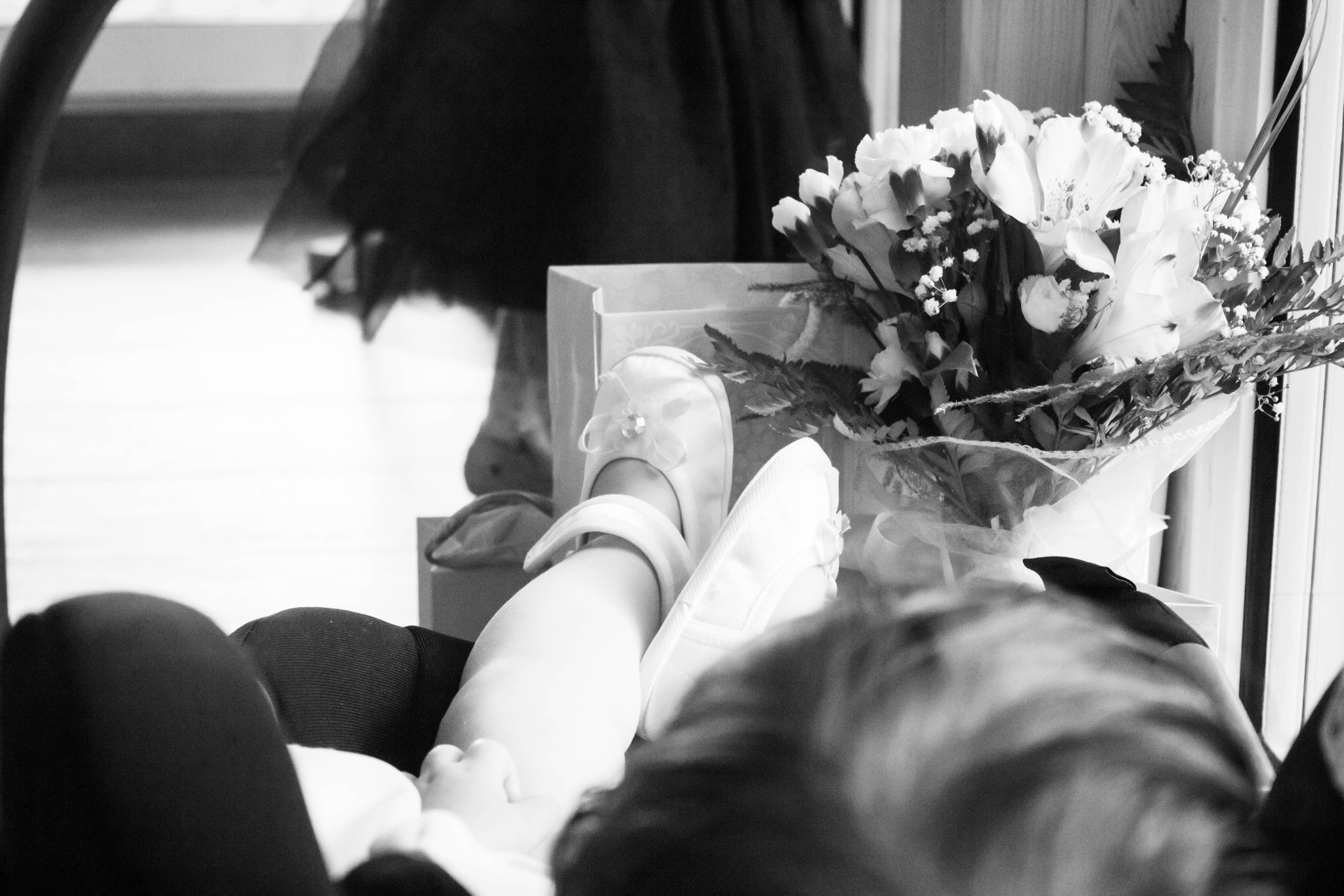 Czarno-białe ujęcie baletek z ozdobnymi kokardkami, bukietu białych kwiatów i odbicia w lustrze, prawdopodobnie przygotowania do uroczystości.