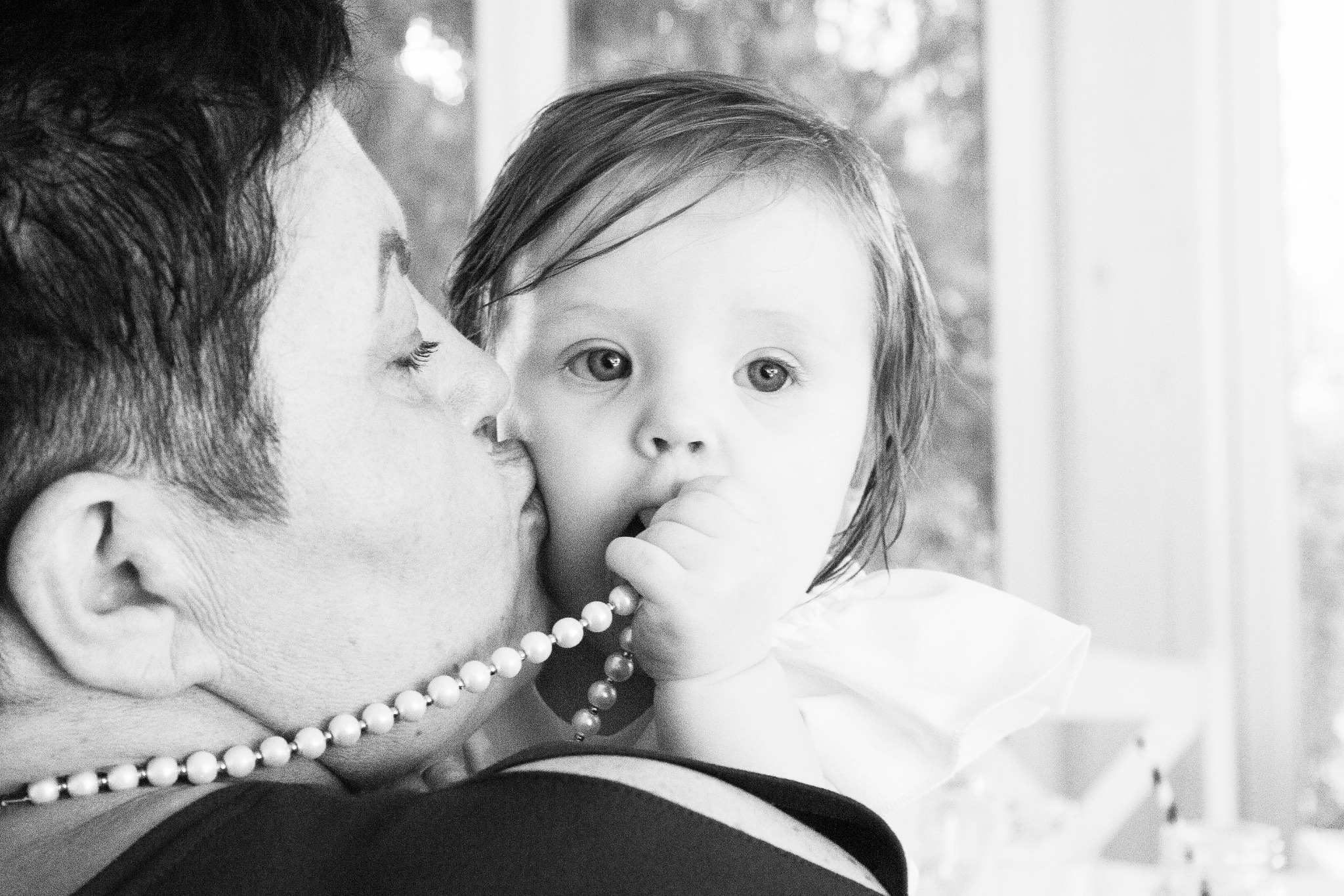 Czarno-białe zdjęcie z Chełma przedstawia matkę całującą w policzek swoje małe dziecko, które trzyma w ręku sznur pereł i patrzy w obiektyw.