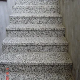 Schody zewnętrzne z szarego kamienia o drobnej fakturze, widok z dołu, z numerem rejestracyjnym pojazdu widocznym w tle.